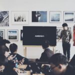 A group of adults attending a casual business presentation in a modern art space, featuring a TV display and framed art.